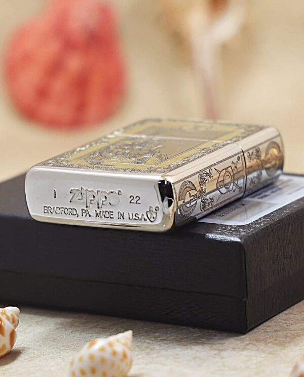 Shiny Zippo lighter with ornate engravings resting on a black box, beachy background and seashells nearby.