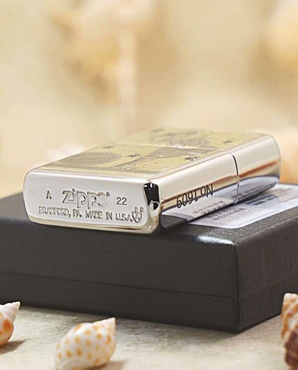 Shiny silver Zippo lighter resting on a black box with small seashells in the foreground.