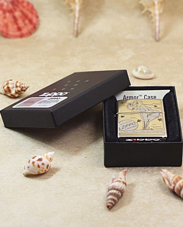 Black presentation box with a brass Zippo lighter featuring a tropical scene, placed among seashells on a beige surface