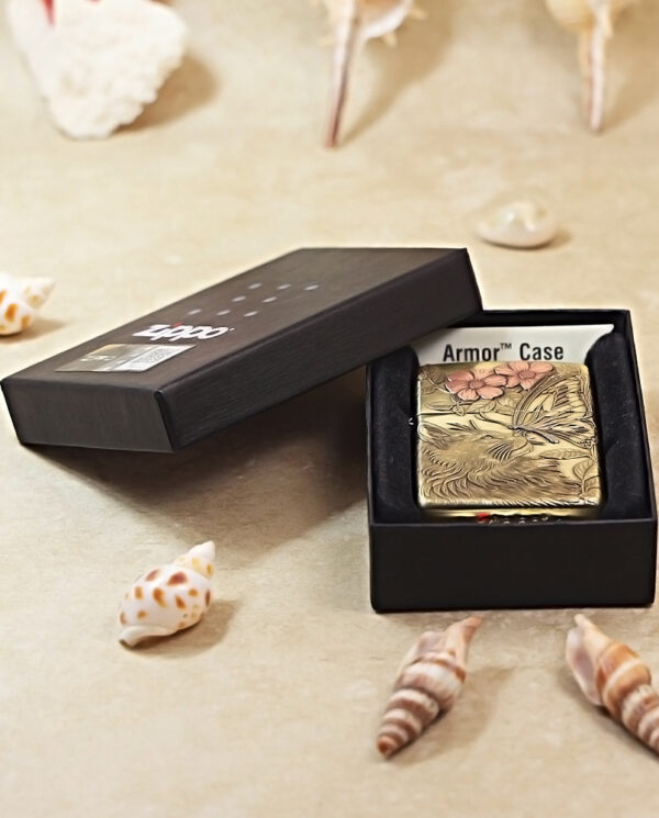 KZ135-06 Brass Zippo-style lighter with floral engraving, shown in an open black presentation box on a beige surface with seashells nearby.