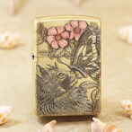 Beige metal lighter with a detailed engraving of a wolf, butterfly, and pink flowers among leaves.