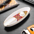 White ceramic boat-shaped ashtray with a colorful floral inlay and gold trim, brand logo visible in the corner.