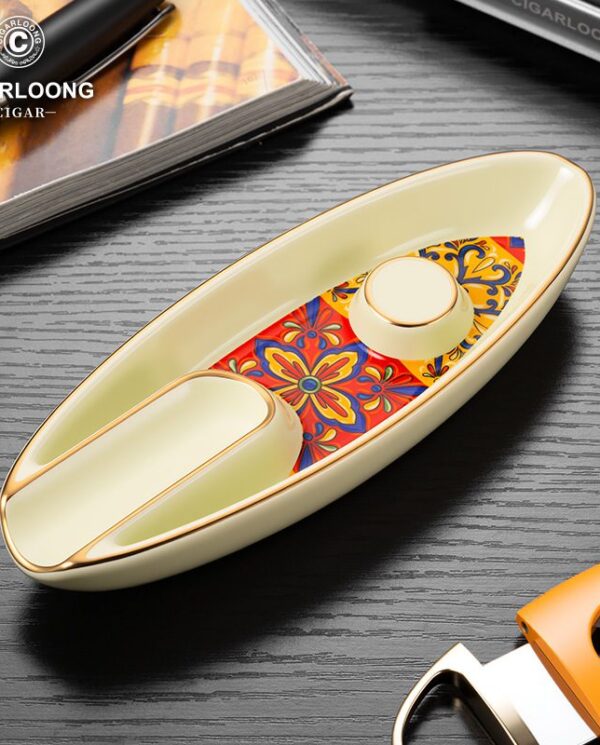 CL016-02 Boat-shaped ceramic ashtray with gold trim and a colorful floral inlay, placed on a dark wood surface with Cigarloong branding in the corner.
