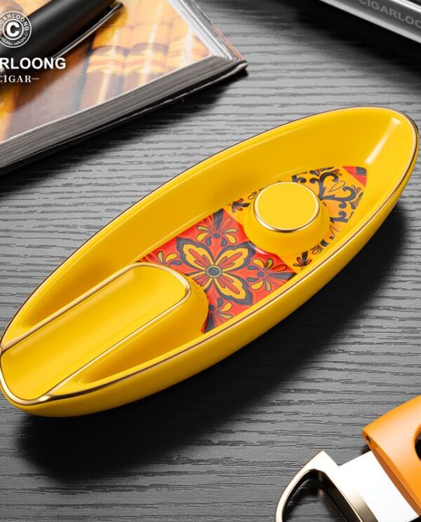 CL016-03 Yellow cigar cutter with a floral inlay on a dark wooden table, beside a cigars box.