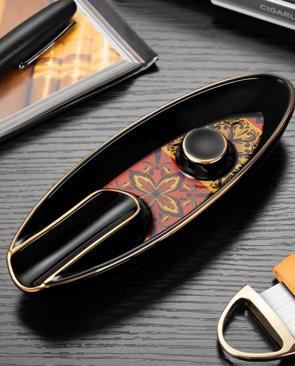 CL016-04 Premium black and gold cigar lighter with an ornate red-and-gold patterned insert, placed on a desk beside a pen and tools
