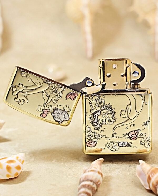 KZ117-02 Gold engraved lighter (Zippo) with floral design, lid open, resting on sand among seashells.