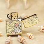 Gold engraved Zippo lighter with cartoon characters, lid open, on a sandy surface among seashells.