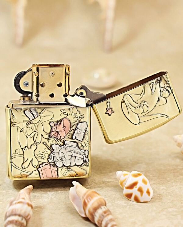 KZ117-03 Gold engraved Zippo lighter with cartoon characters, lid open, on a sandy surface among seashells.