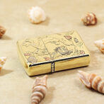Gold decorative lighter with engraved dragon and flowers, set on a sandy surface with seashells scattered around.
