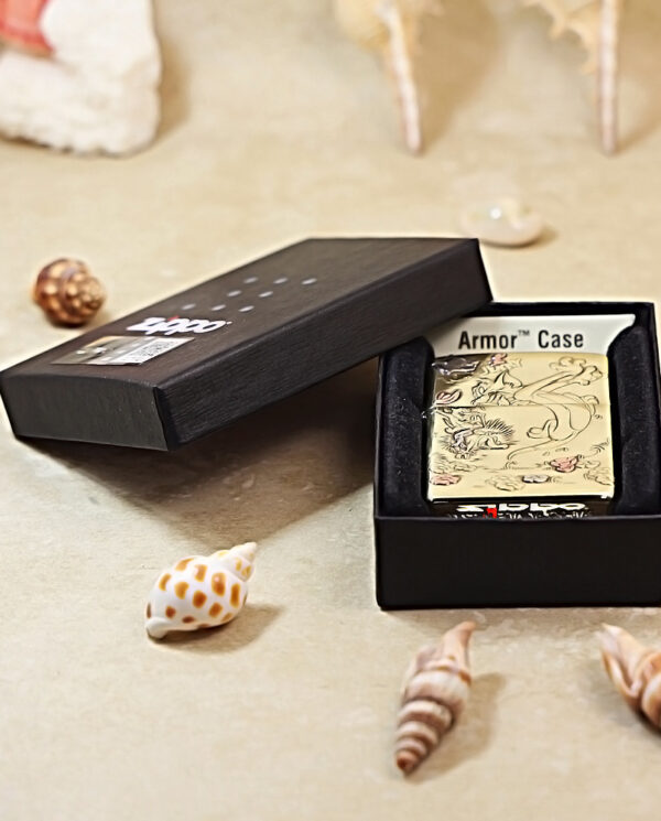 KZ117-06 Black gift box opened to reveal a beige Zippo-style lighter with dragon artwork labeled Armor Case, resting on a sand surface among seashells.