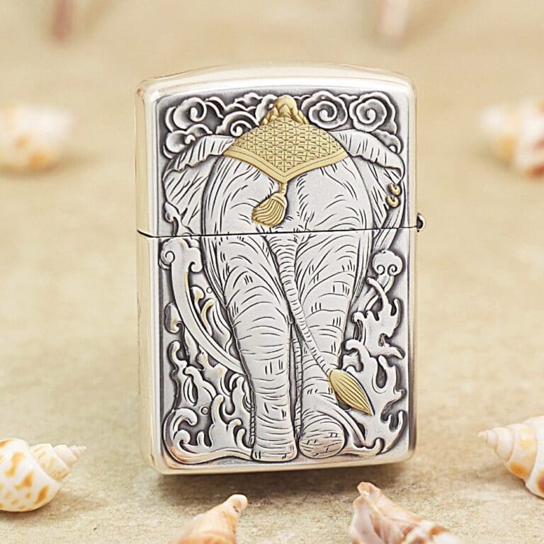 Silver Zippo-style lighter with an embossed elephant design, gold headdress detail, surrounded by ornate clouds and patterns.