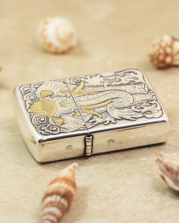 KZ127-02 Ornate silver lighter with a dragon engraving on a sandy surface, surrounded by seashells