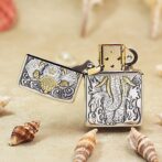 Open, ornate metal lighter with a dragon engraving and gold accents on a sandy surface, surrounded by seashells.