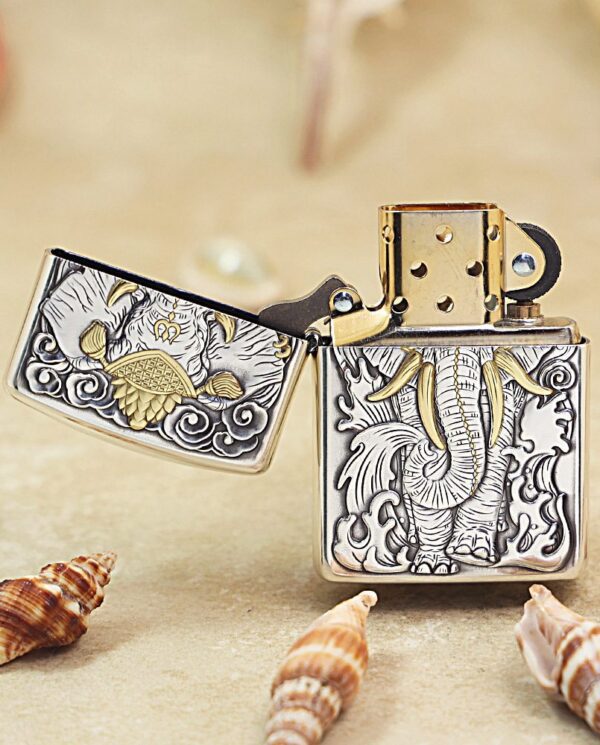 KZ127-03 Open, ornate metal lighter with a dragon engraving and gold accents on a sandy surface, surrounded by seashells.