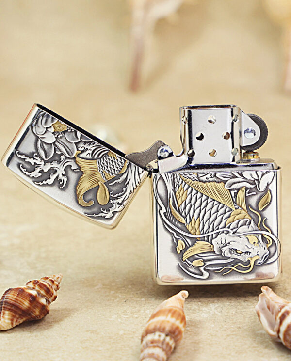 KZ136-02 Silver engraved lighter with a gold dragon design, open lid on a sandy surface with shells.