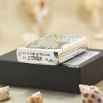 Close-up of a metallic Zippo lighter with an ornate design resting on a black box, with seashells in the foreground.