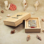 Boxed Zippo lighter in a light wood display box on a sandy shell backdrop with shells around it