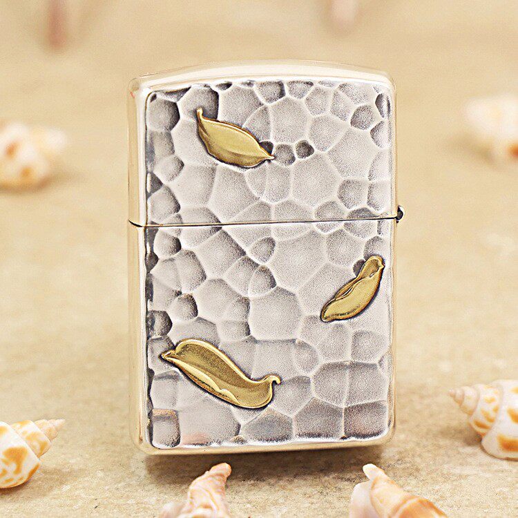 Metallic lighter with a textured, pebble-like surface and gold leaf accents on a sandy background.