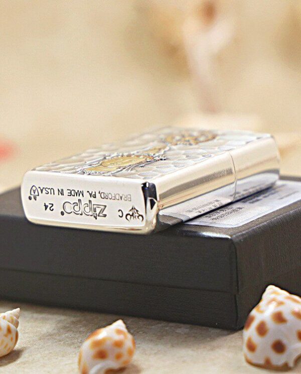KZ148-03 Silver patterned Zippo lighter resting on a black box, with seashells on a sandy surface nearby