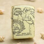 Gold Zippo lighter with vintage illustration and the text 'Since 1932' and 'American Classic' displayed on the front, resting on a sandy surface.