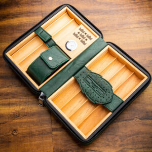 Green leather travel humidor with two wooden compartments and a pocket strap, shown open on a wooden surface.