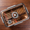 Open cigar humidor on a wooden table with neatly arranged cigars, a circular lock, and a digital hygrometer showing conditions