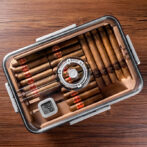 Open cigar humidor on a wooden table with neatly arranged cigars, a circular lock, and a digital hygrometer showing conditions