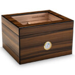 Wooden cigar humidor with a glass top window and a gold-rimmed hygrometer on the front, used to store cigars.