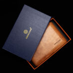 Blue gift box with gold logo opens to reveal a brown leather cigar case inside an orange-lined box with a black interior.