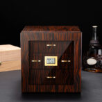 Wooden cigar humidor with glass front and gold handles, digital humidity display reading 70% inside a dark room.
