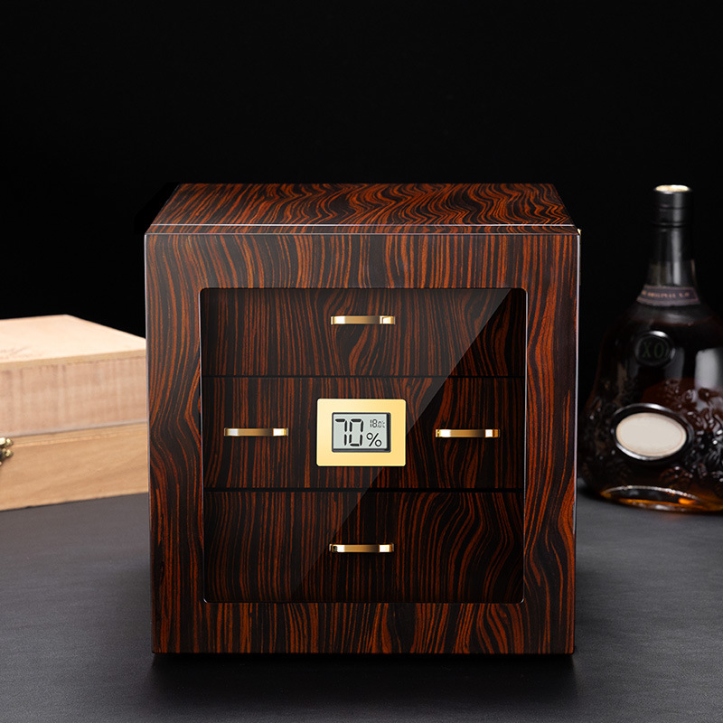 Wooden cigar humidor with glass front and gold handles, digital humidity display reading 70% inside a dark room.
