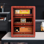 Wooden cigar humidor with glass panels showing cigars and a digital hygrometer reading 57% humidity.