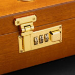 Gold-colored combination padlock on a wooden case or box, with three rotating dials set to 0-0-0 and a brass latch.