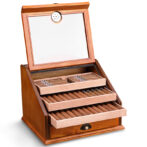 Open wooden cigar humidor with cigars neatly arranged in sliding trays and a bottom drawer, under a glass lid with a mirror inside