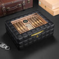 Black quilted leather cigar humidor with a glass lid, showing cigars neatly arranged inside and a small hygrometer visible on the top panel.