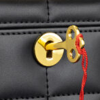 Gold-colored key hooked to a latch on a black leather bag with a red string attached for security.