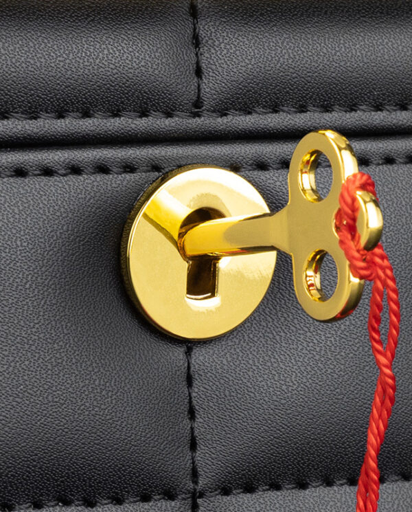 CH014-03 Gold-colored key hooked to a latch on a black leather bag with a red string attached for security.