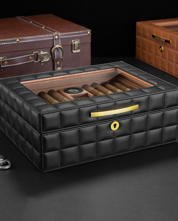 CH014 Black quilted leather cigar humidor with a glass lid, holding several cigars and a small humidifier disk inside, gold front plate visible.