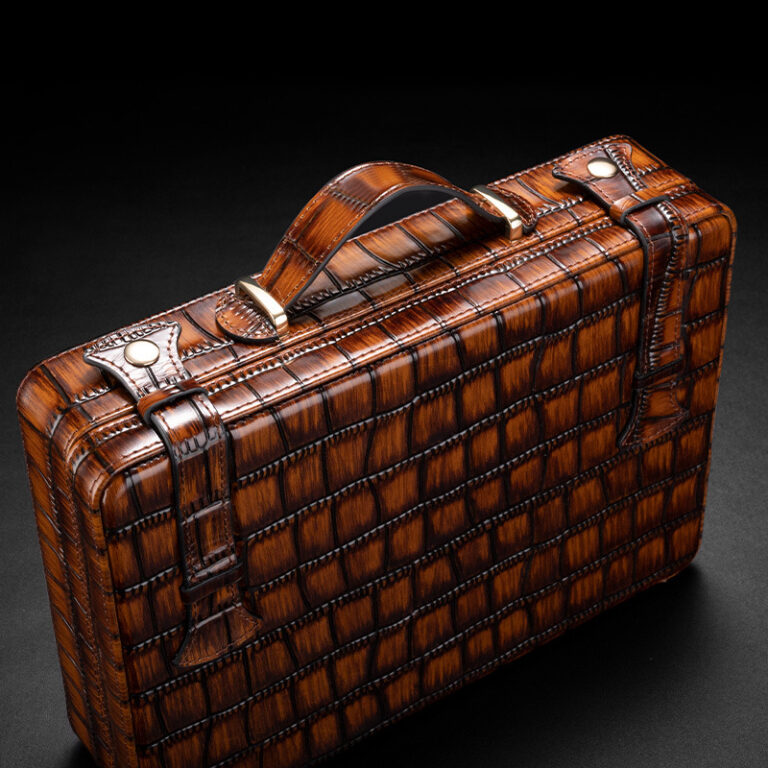 Brown textured leather briefcase with a crocodile pattern, brass hardware, and a top handle on a dark background
