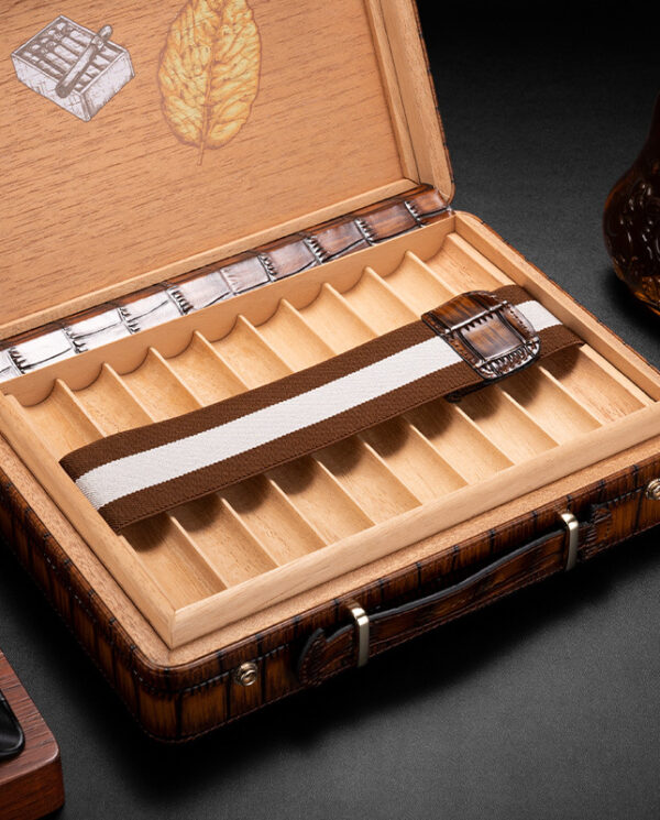 CH015-03 Opened wooden cigar box with multiple divider slots; a brown-and-white striped strap rests across the tray; a bottle sits nearby on the right.