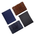 Four leather accessories on a white background: brown crocodile wallet, navy crocodile wallet, dark blue folder, and black drawstring pouch.