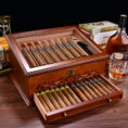 Open wooden cigar humidor with cigars arranged in rows; drawer pulled out showing more cigars.