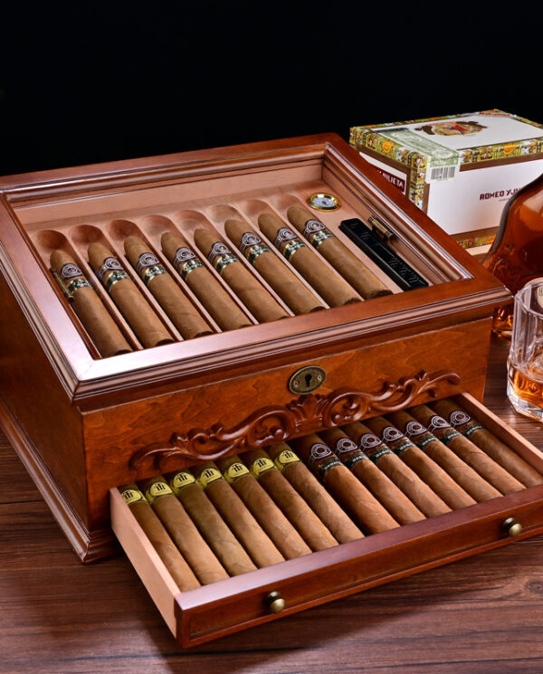 Open wooden cigar humidor with cigars arranged in rows; drawer pulled out showing more cigars.