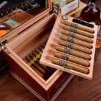 Open cedar cigar humidor with two drawers and rows of cigars, one tray lifted for viewing.