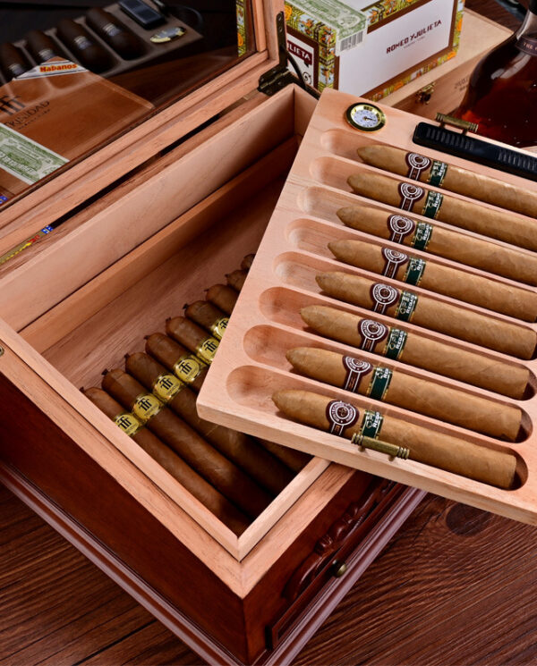 Open cedar cigar humidor with two drawers and rows of cigars, one tray lifted for viewing.