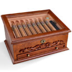 Ornate mahogany cigar humidor with glass top, showing a row of cigars and a small drawer beneath
