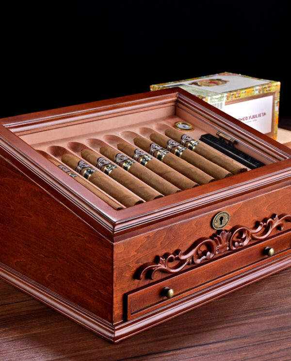 Polished wooden cigar humidor opened to reveal a row of cigars resting in a built-in tray with a key lock and decorative carving on the front panel.
