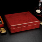 Polished red-brown wooden box on a black surface, with a bottle of Hennessy cognac in the background.