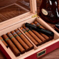 Cigar humidor open with multiple cigars lined up, a cutter resting on top, and a bottle of cognac nearby.