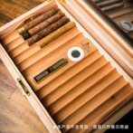 Wooden cigar humidor opened to reveal several cigars, a digital hygrometer, and a humidifying slider inside.